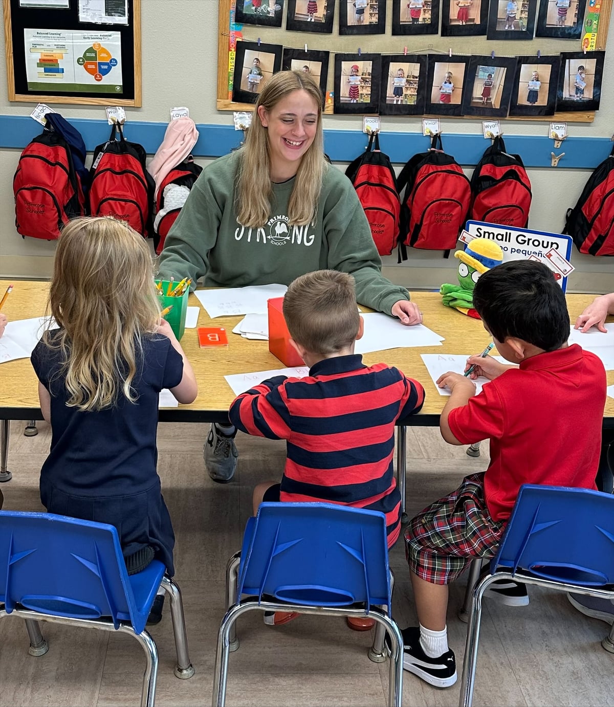 Preschool teacher guiding three students during a writing table lesson plan at Primrose School of Eagan