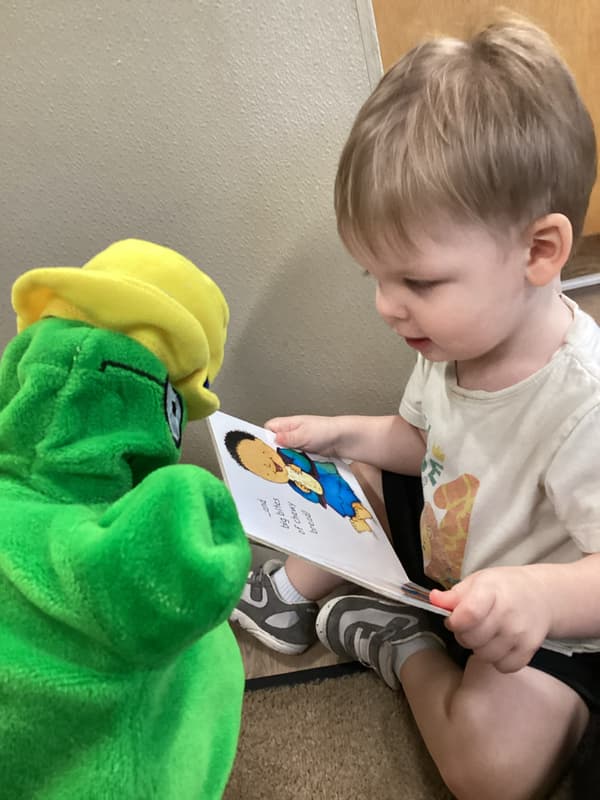 Infant reading a book with Primrose Puppet Og at Primrose School North Lewisville Lewisville TX