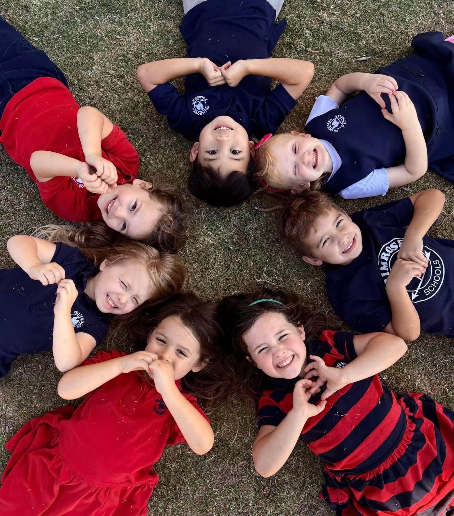 Children laying in a circle smiling holding up hearts