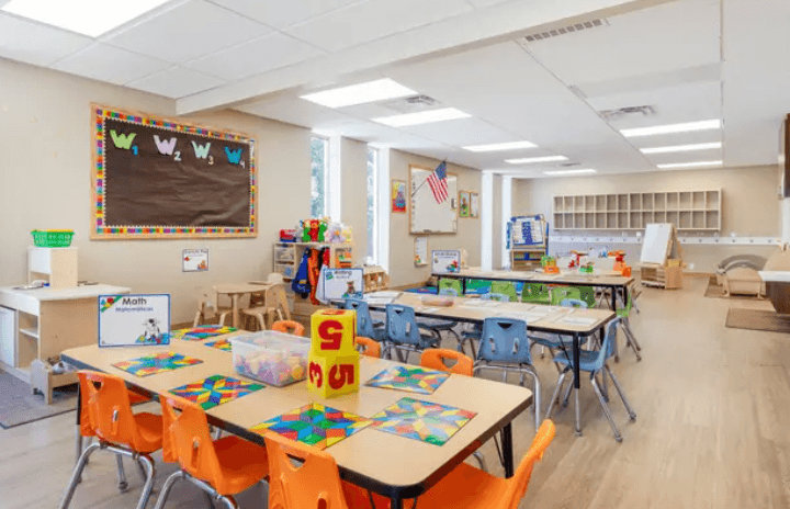 Bright colorful classroom, large windows, and bulletin board. Educational toys set out on tables.