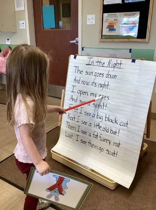 Preschool student using a pointer to track words on a poetry chart during a shared reading lesson