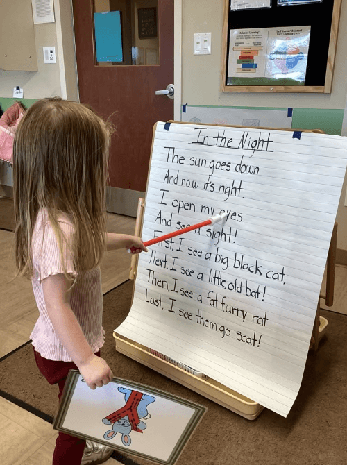 Preschool student using a pointer to track words on a poetry chart during a shared reading lesson