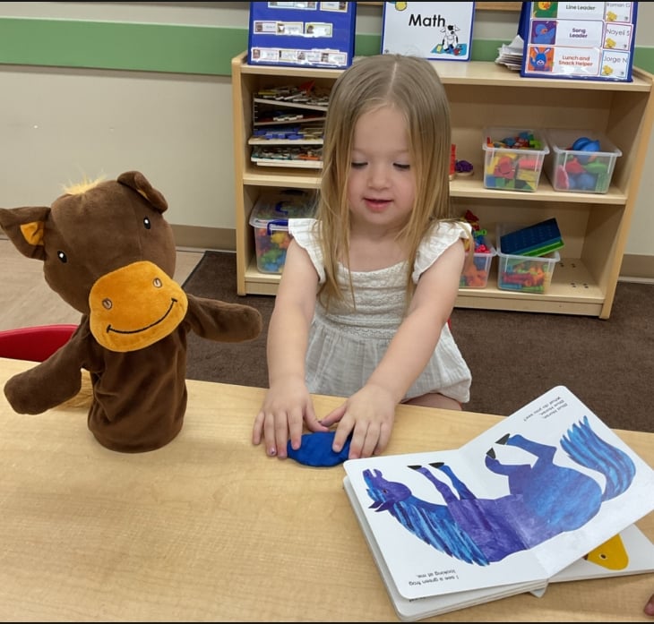 Young student using blue modeling dough while exploring a storybook activity that encourages imagination, literacy, and creative expression.
