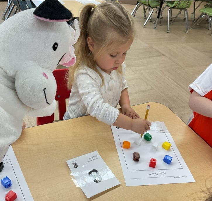 Preschool student counting colorful cubes and recording observations on a math worksheet during a hands-on classroom learning activity.