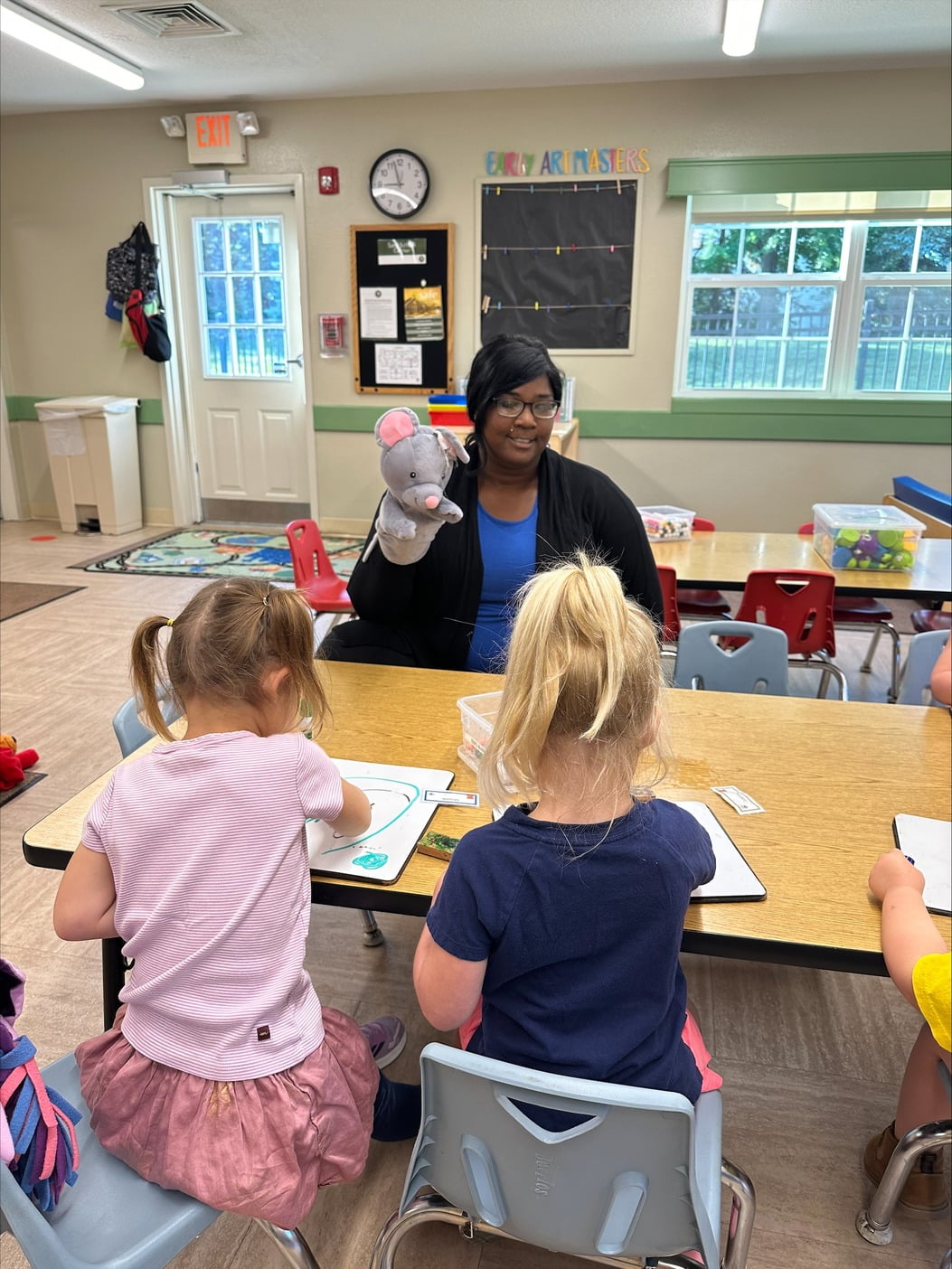 Warm-Hearted Preschool Teacher at Primrose School of Eagan Sits with Two Engaged Preschoolers at a Classroom Table, Guiding Artistic Exploration and Fostering Imagination in an Enriching Early Education Setting