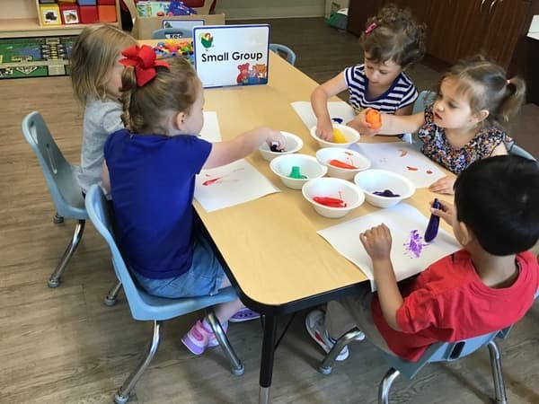 Four preschoolers seated at a small table, painting with colorful watercolors during a small-group art activity.