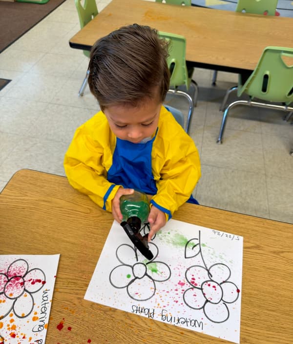 Child using a spray bottle to create colorful flower artwork during a sensory-based painting activity.