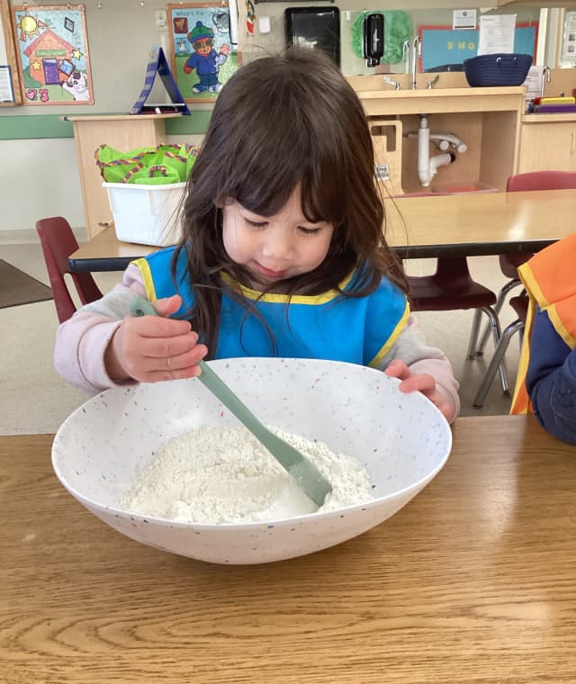 Preschool child stirring ingredients in a mixing bowl during a cooking activity at Primrose School of Thornton