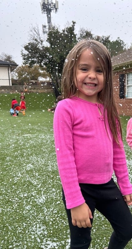 little girl in pink shirt on playground with fake snow falling
