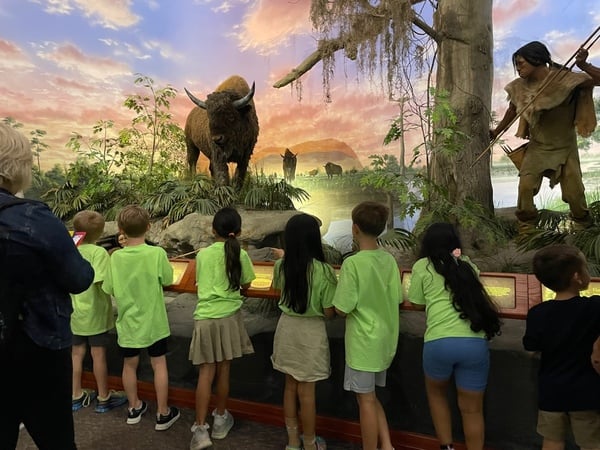 Children exploring a museum exhibit featuring prehistoric wildlife and early human history during an educational field trip experience.