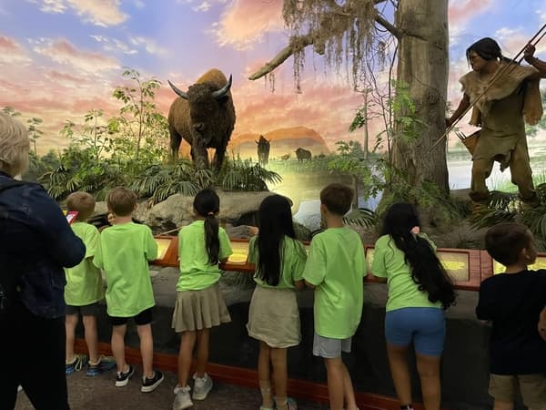 Children exploring a museum exhibit featuring prehistoric wildlife and early human history during an educational field trip experience.