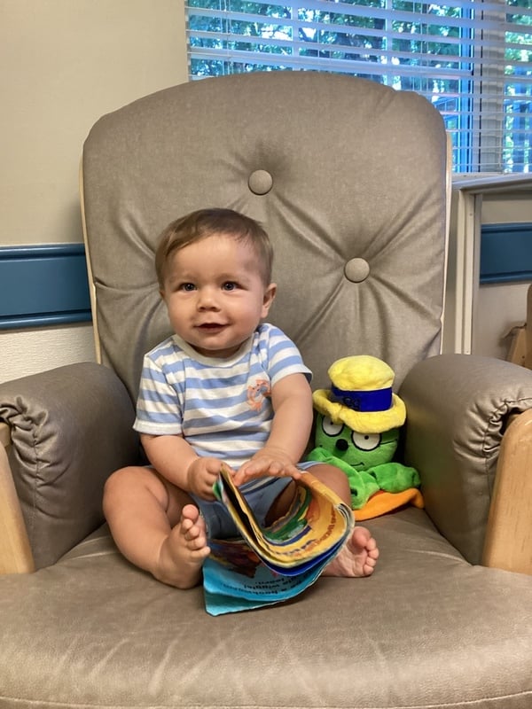 Baby sitting on chair, holding a book with our Og puppet