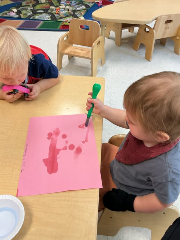 Child painting with paint brush while sitting at the table