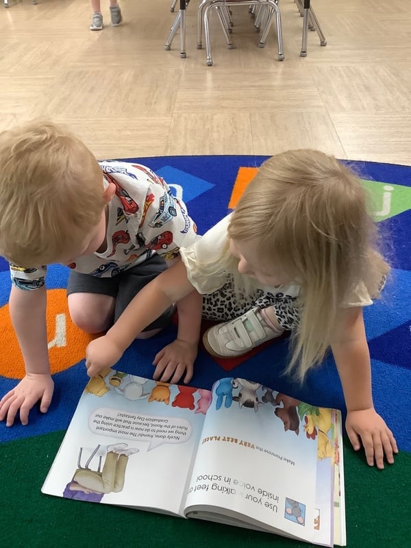 Two preschool children reading a picture book together on a colorful classroom rug at Primrose School, building early literacy and social-emotional development.