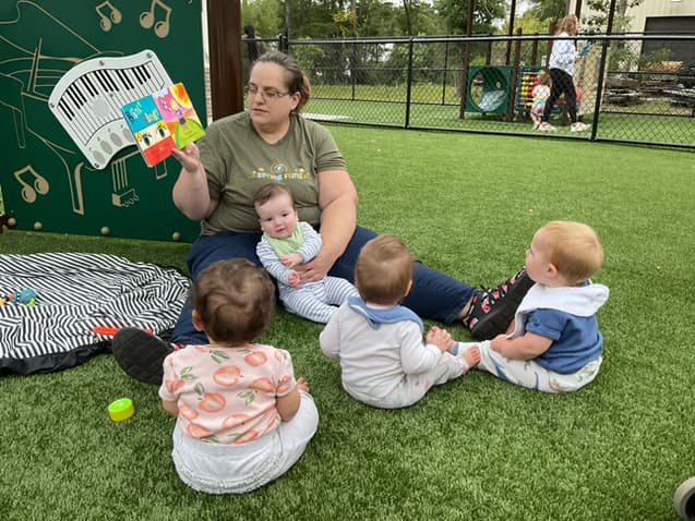 Ms. Jen reads to the babies outside