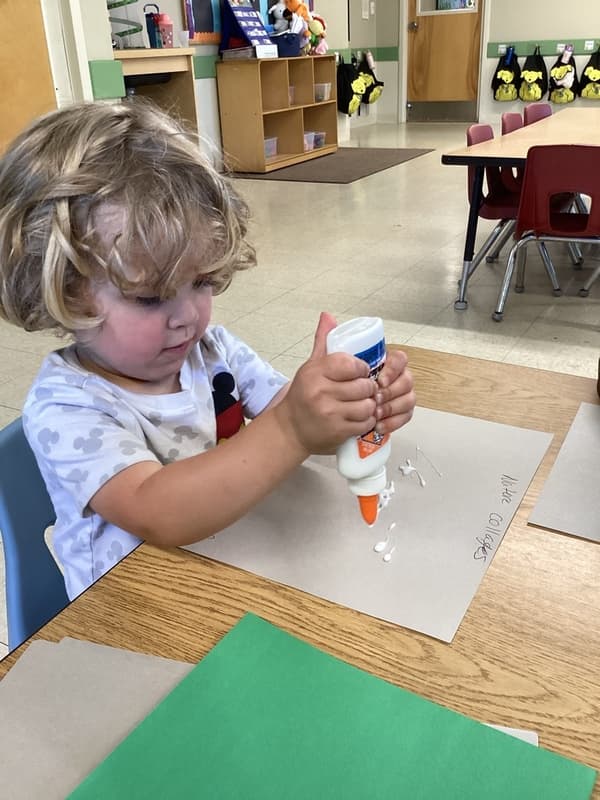 Young child practicing hand strength and coordination while applying glue for a classroom collage project.