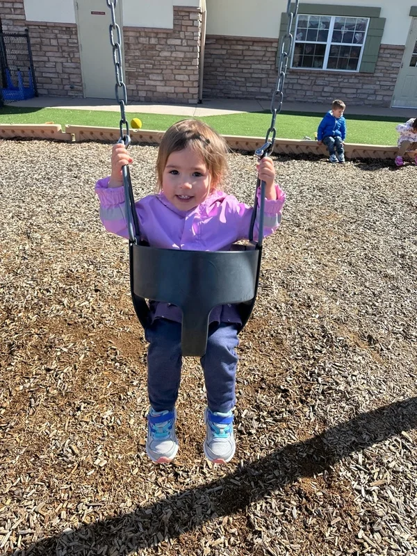 A child having fun swinging outside on the playground at Primrose school of north colorado springs