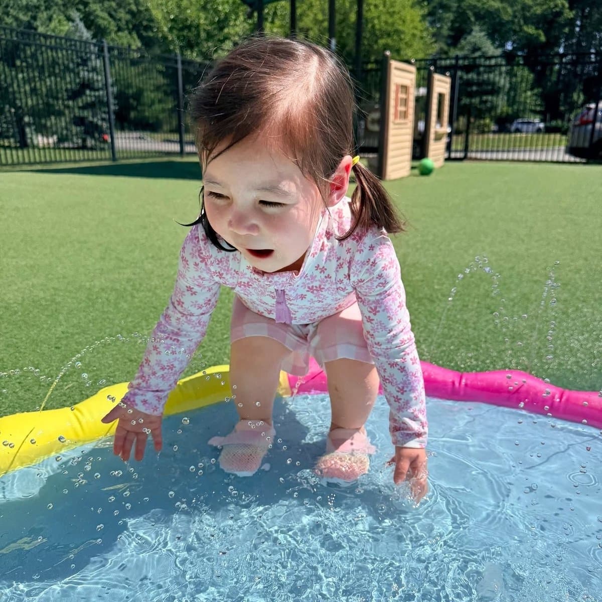 Toddler girl splashing in outdoor water play area at Primrose School of Chelmsford early preschool in Chelmsford, MA