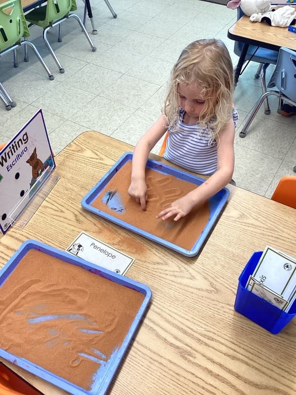 Preschool student tracing letters and shapes in a sensory writing tray to develop early handwriting and fine motor skills.