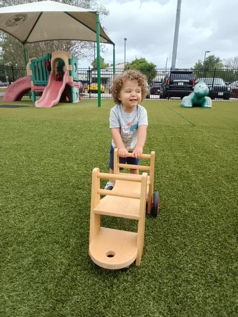 child pushes a bike on the playground, focusing on gross motor skills