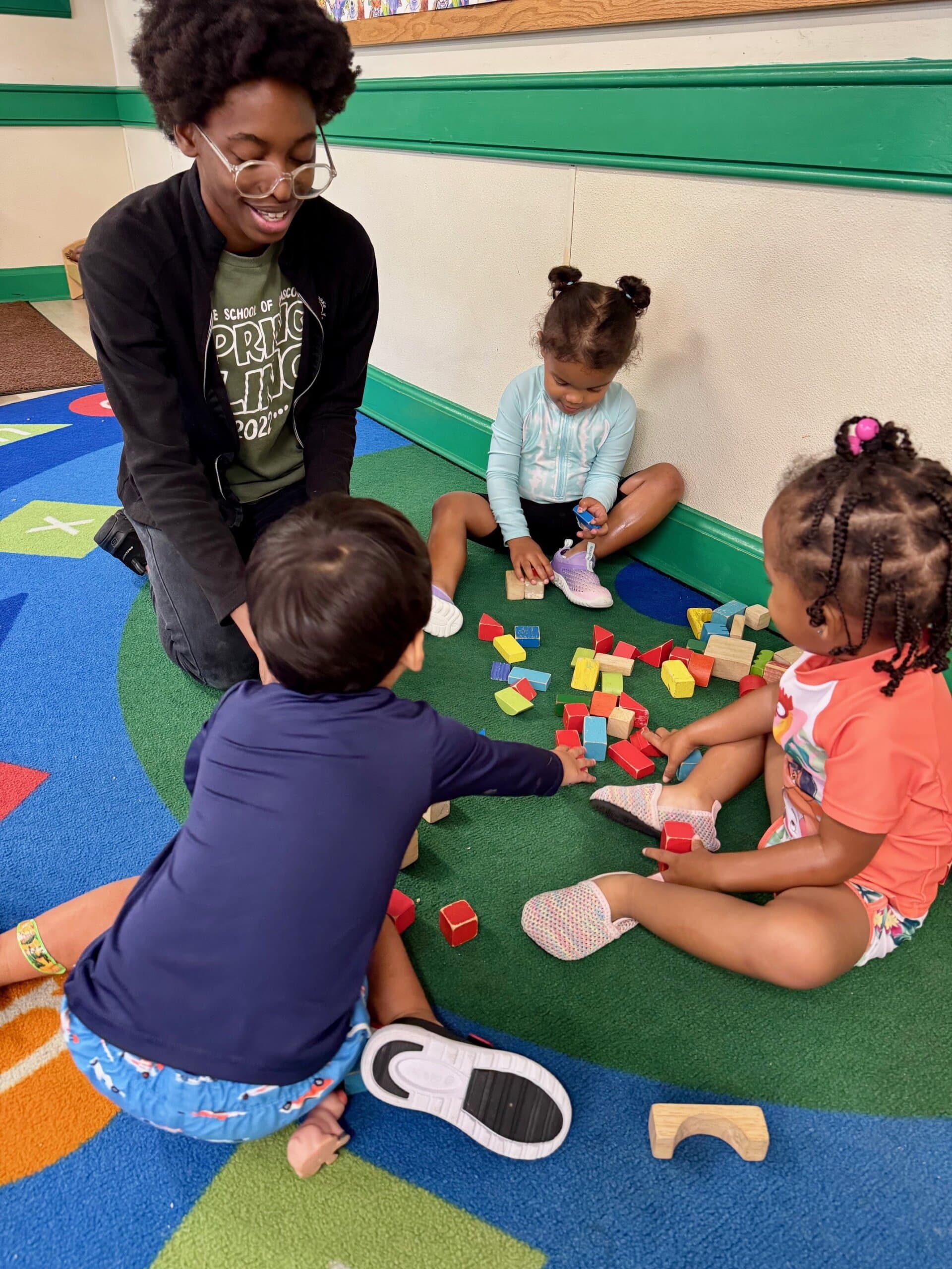 Preschool students playing with building blocks near a teacher, engaging in play that supports creativity and early learning development