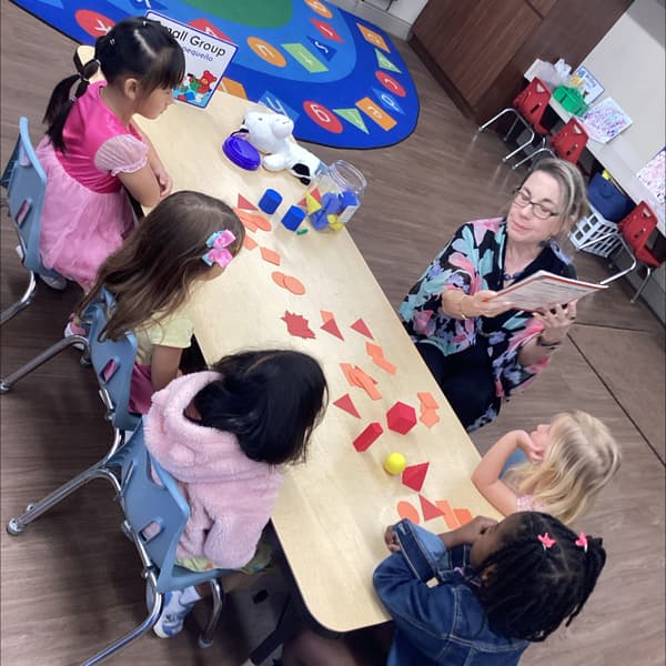 Teacher leads small group math activity sorting red shapes at table to support fine motor and shape recognition skills