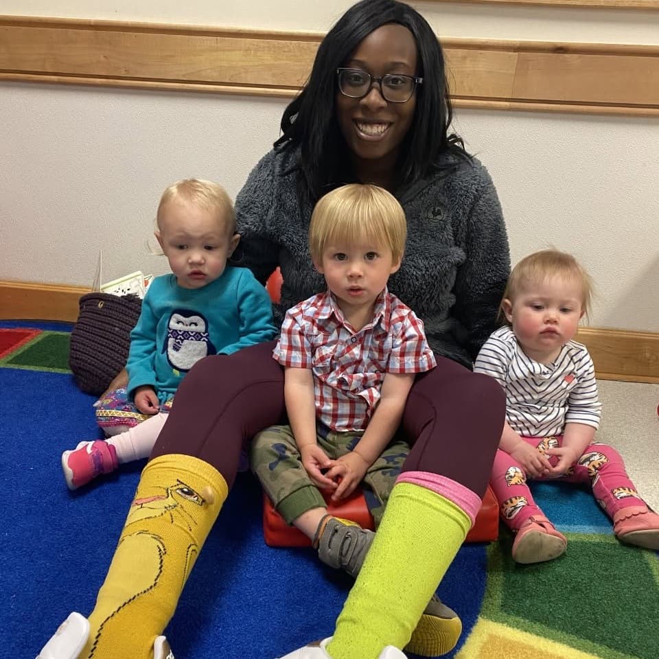 Teacher sitting with three young children on a classroom rug at Primrose School at Highlands Ranch Business Park in Highlands Ranch, Colorado, supporting nurturing relationships and early social development.