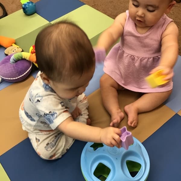 Two infants playing with shapes trying to place them into the matching shape.