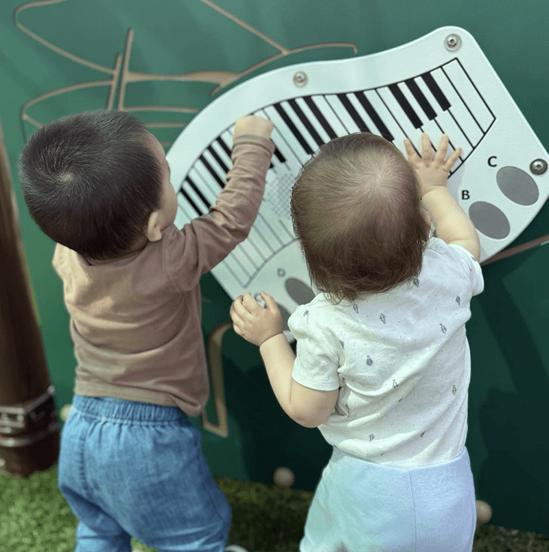 Two infants exploring a musical keyboard wall activity at Primrose School of Chelmsford infant daycare in Chelmsford, MA