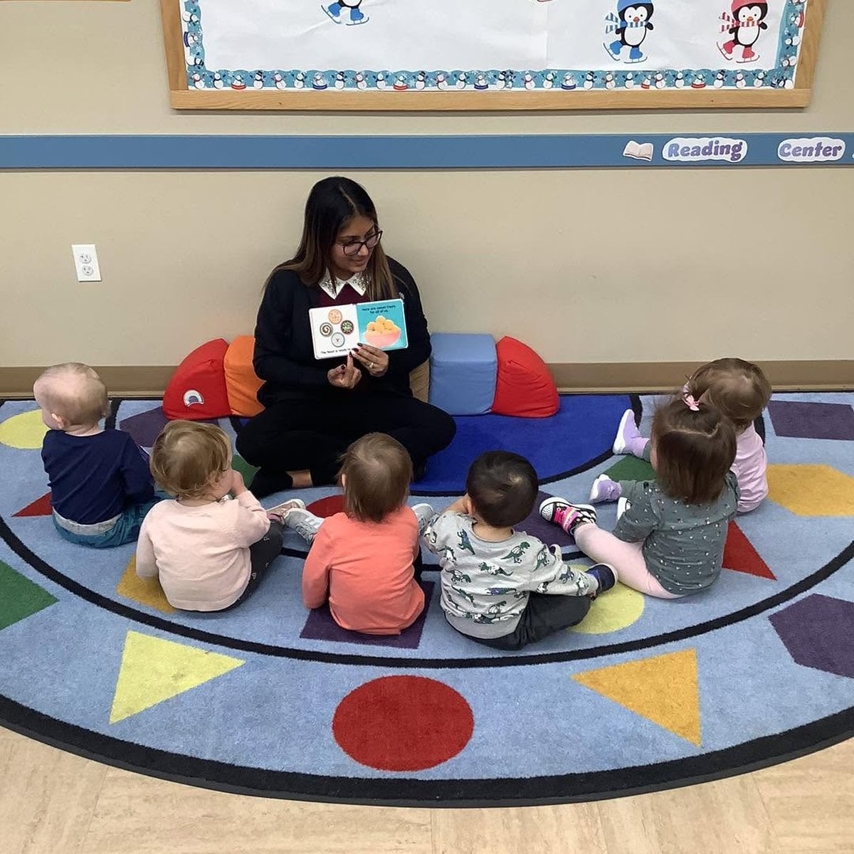 Teacher reading a book to infants gathered on the classroom rug at Primrose School of Woburn infant daycare in Woburn, MA