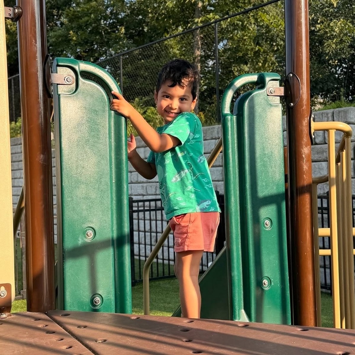 Pre-K child smiling while climbing on the outdoor playground structure at Primrose School of Woburn, MA