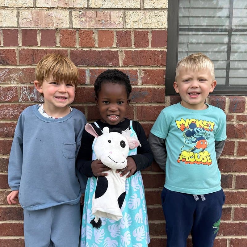 Three preschool children smiling together outdoors at Primrose School at Highlands Ranch Business Park in Highlands Ranch, CO.