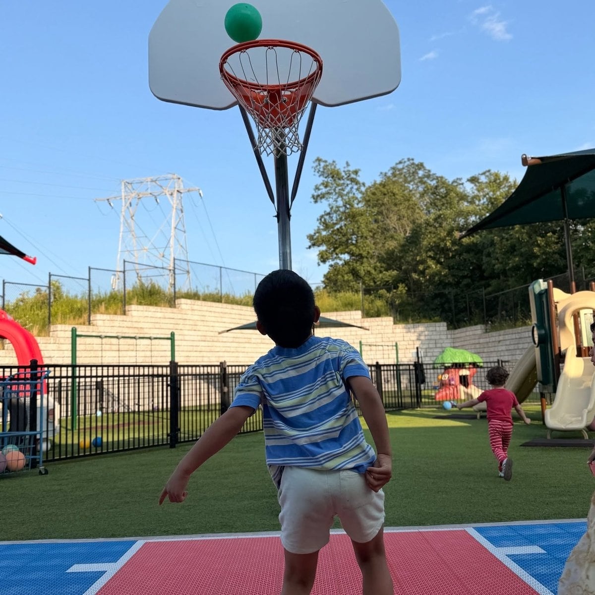 Preschool Pathways child shooting a basketball on the outdoor playground at Primrose School of Woburn, MA