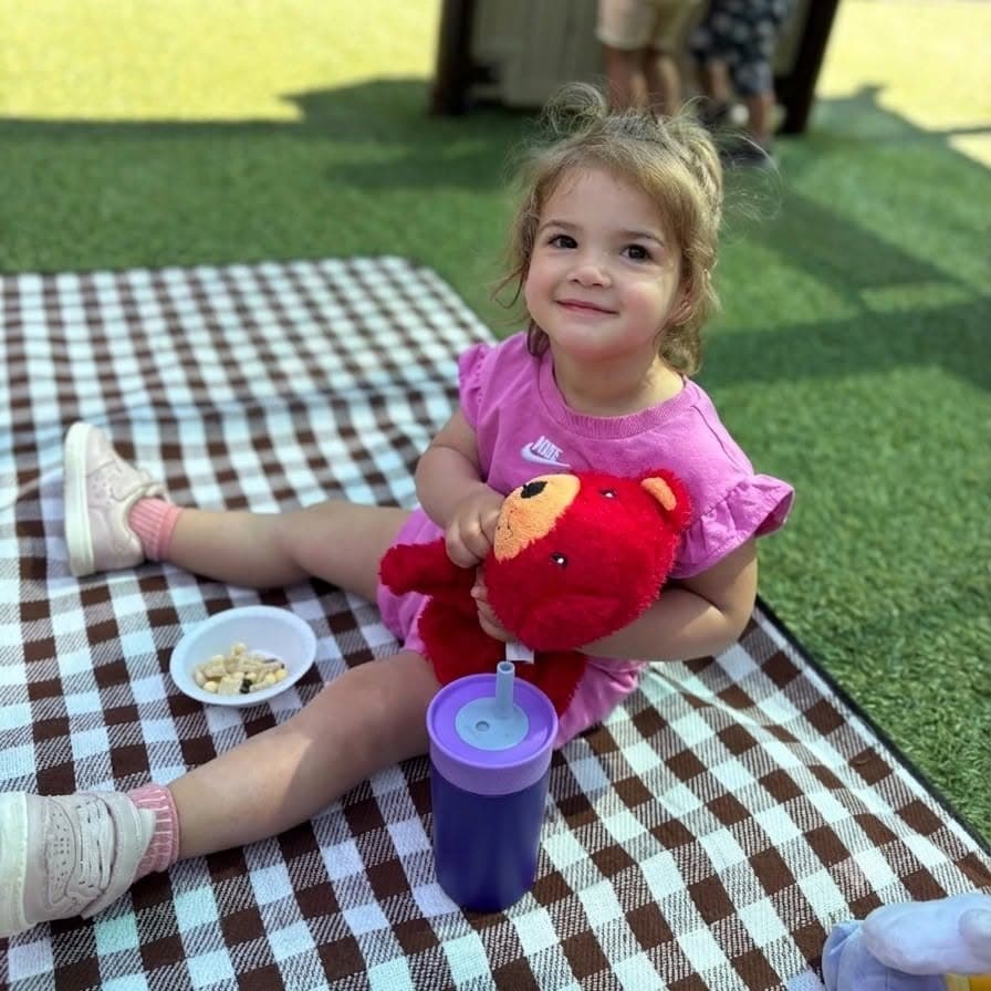 Preschool girl enjoying outdoor snack time on a picnic blanket at Primrose School of Chelmsford preschool in Chelmsford, MA
