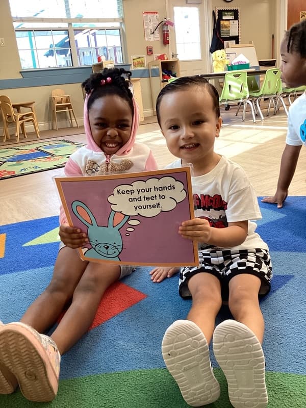 Two Preschool children hold up a Rules of the Roost card during morning circle time