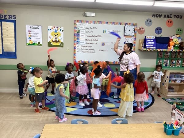 Teacher leads a group of children waving scarves around during music time
