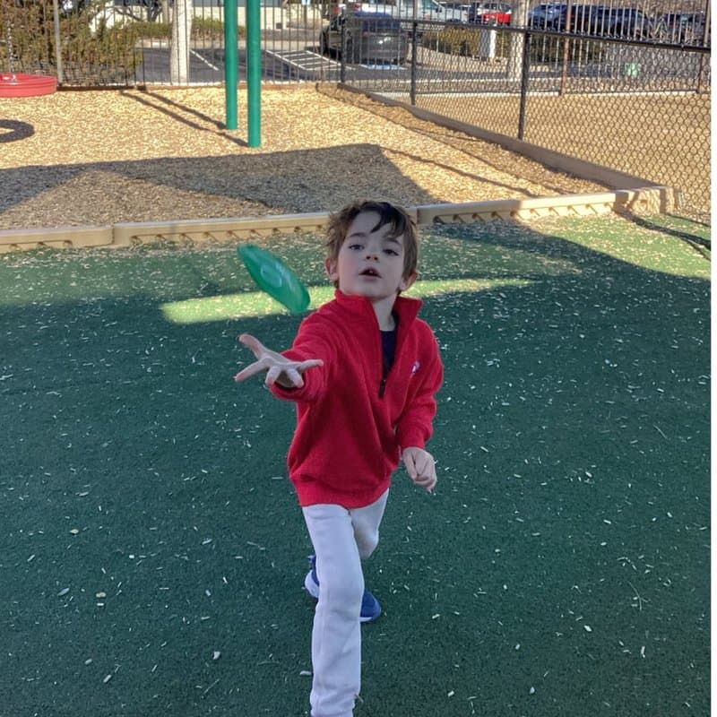 Child tossing a green flying disc during outdoor play at Primrose School at Highlands Ranch Business Park in Highlands Ranch, CO.