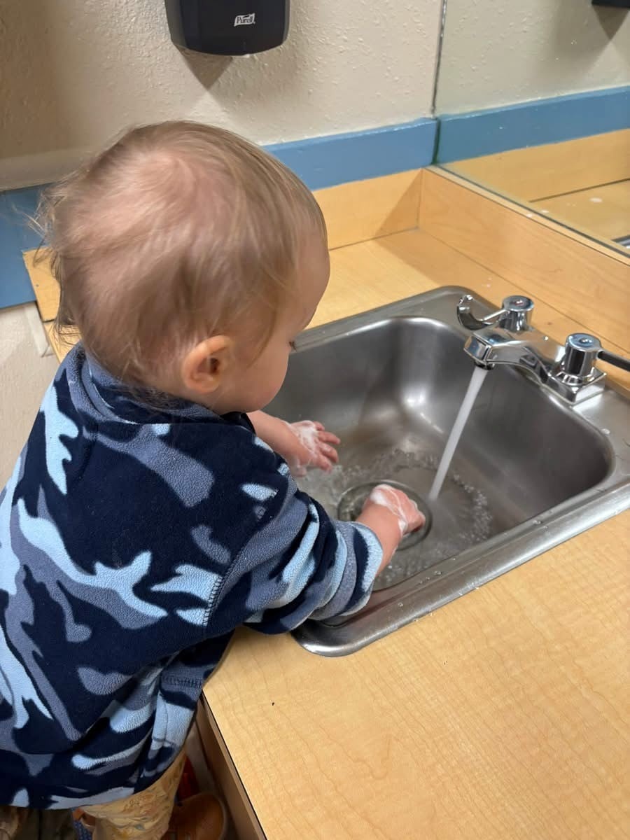 toddler boy washing his hands by himself in a sink