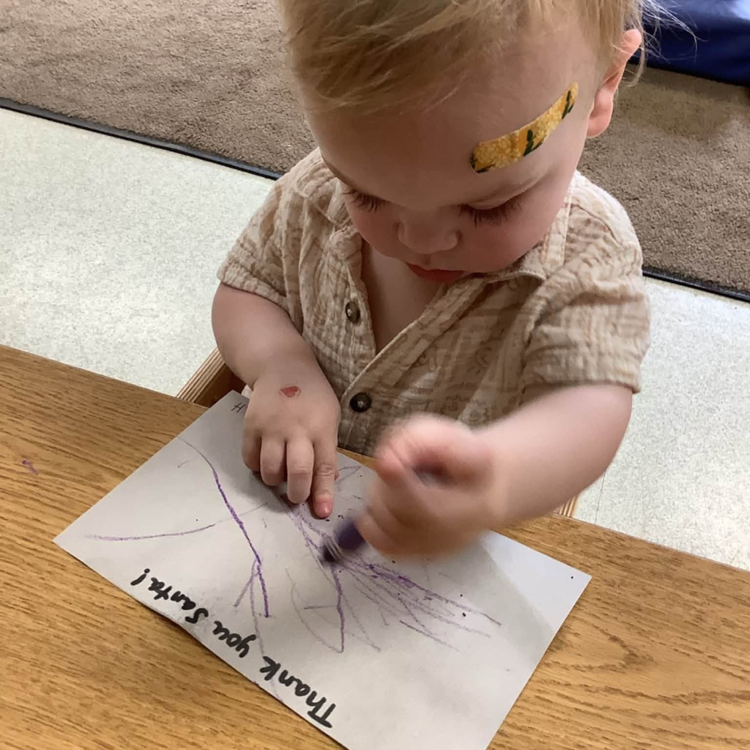 Toddler drawing with a purple crayon during a hands-on classroom activity at Primrose School at Highlands Ranch Business Park, supporting creativity and fine motor development.