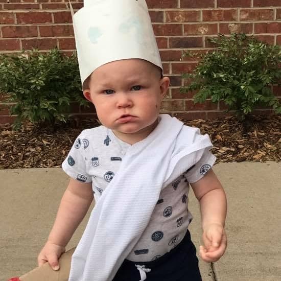 Toddler wearing a handmade paper hat outdoors at Primrose School at Highlands Ranch Business Park, participating in a creative early childhood activity.