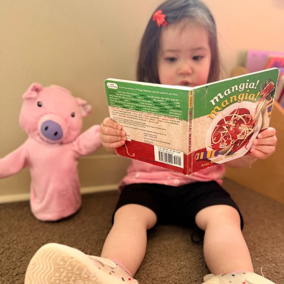 Toddler girl reading a book with a stuffed pig during story time at Primrose School of Chelmsford toddler daycare in Chelmsford, MA