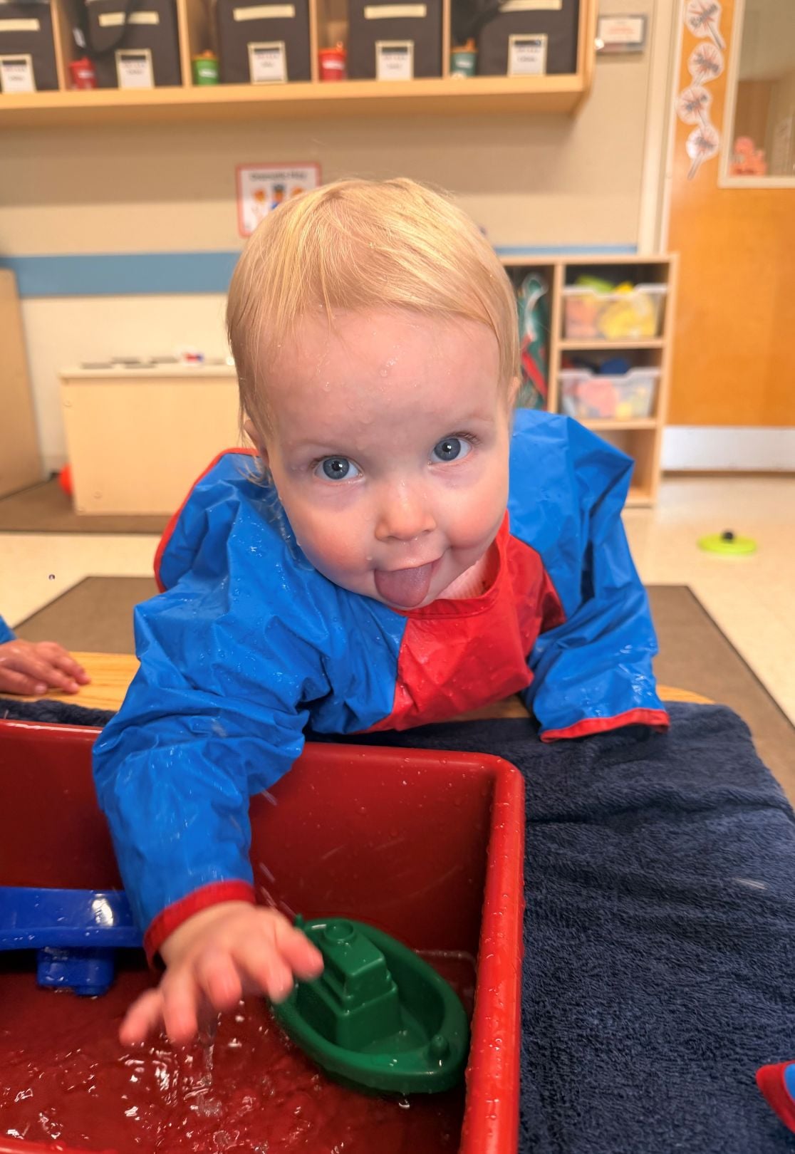toddler girl playing in a bucket of water with floating toy boats