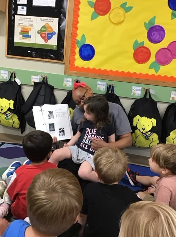 child sitting on teacher's lap reading a book