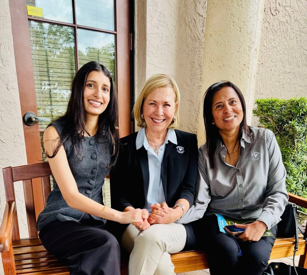 three women sitting on a bench two in gray shirts one in blue