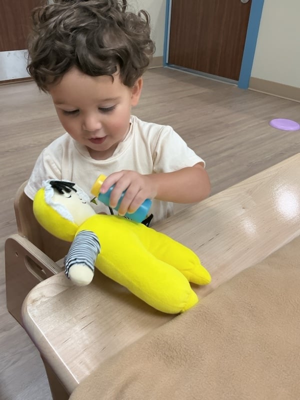little boy with yellow baby doll sitting at a table