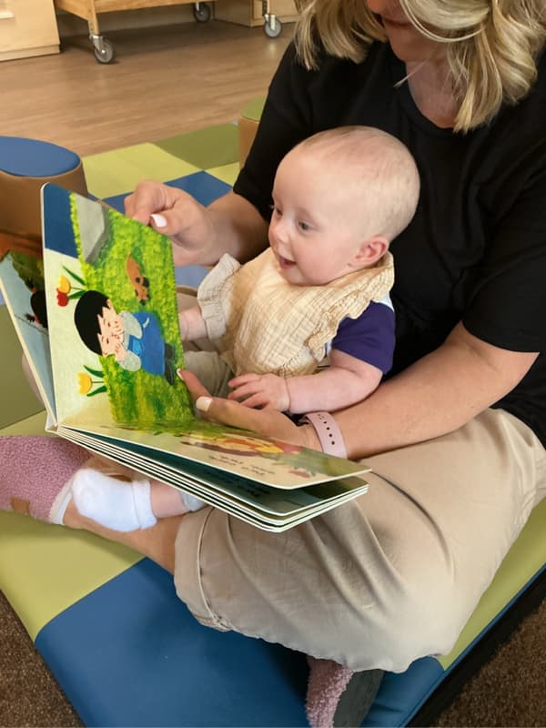An infant sitting in a classroom, exploring a picture book during reading time at Primrose School of Forest Hill, a preschool in Forest Hill, Maryland