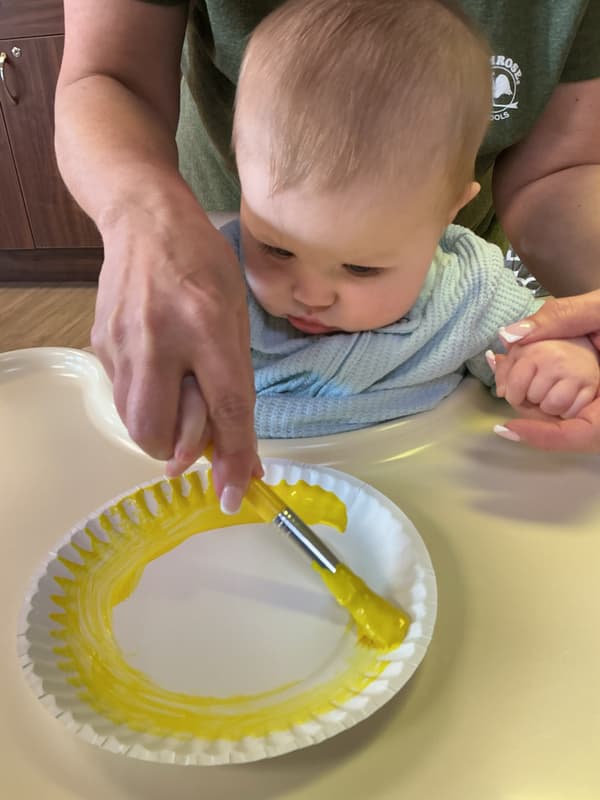 An infant at Primrose School of Forest Hill engaging in a nurturing classroom environment, exploring sensory toys and interacting with a teacher to support early development.