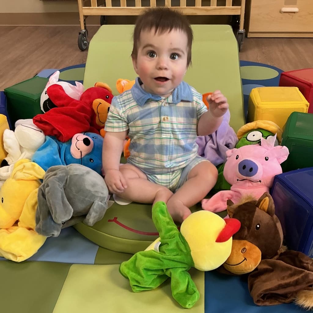 Baby smiling and playing with Primrose Friends character toys in a nurturing infant classroom at Primrose School