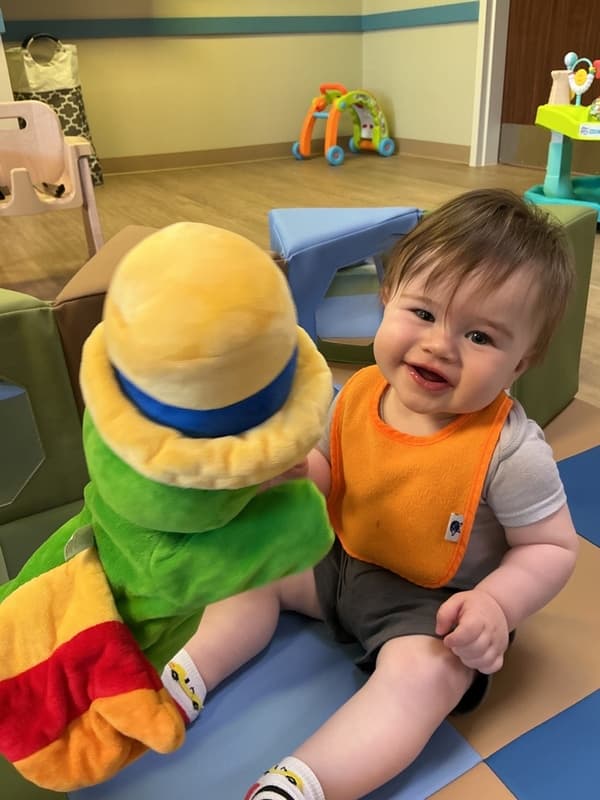 Baby playing with a Primrose Friend plush toy Og the Bookworm during an infant classroom learning activity at Primrose School