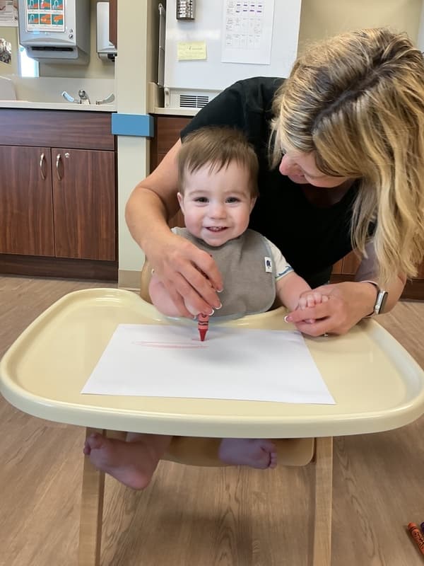 Young infant participating in a sensory art activity with teacher support at Primrose School of Forest Hill in Maryland.